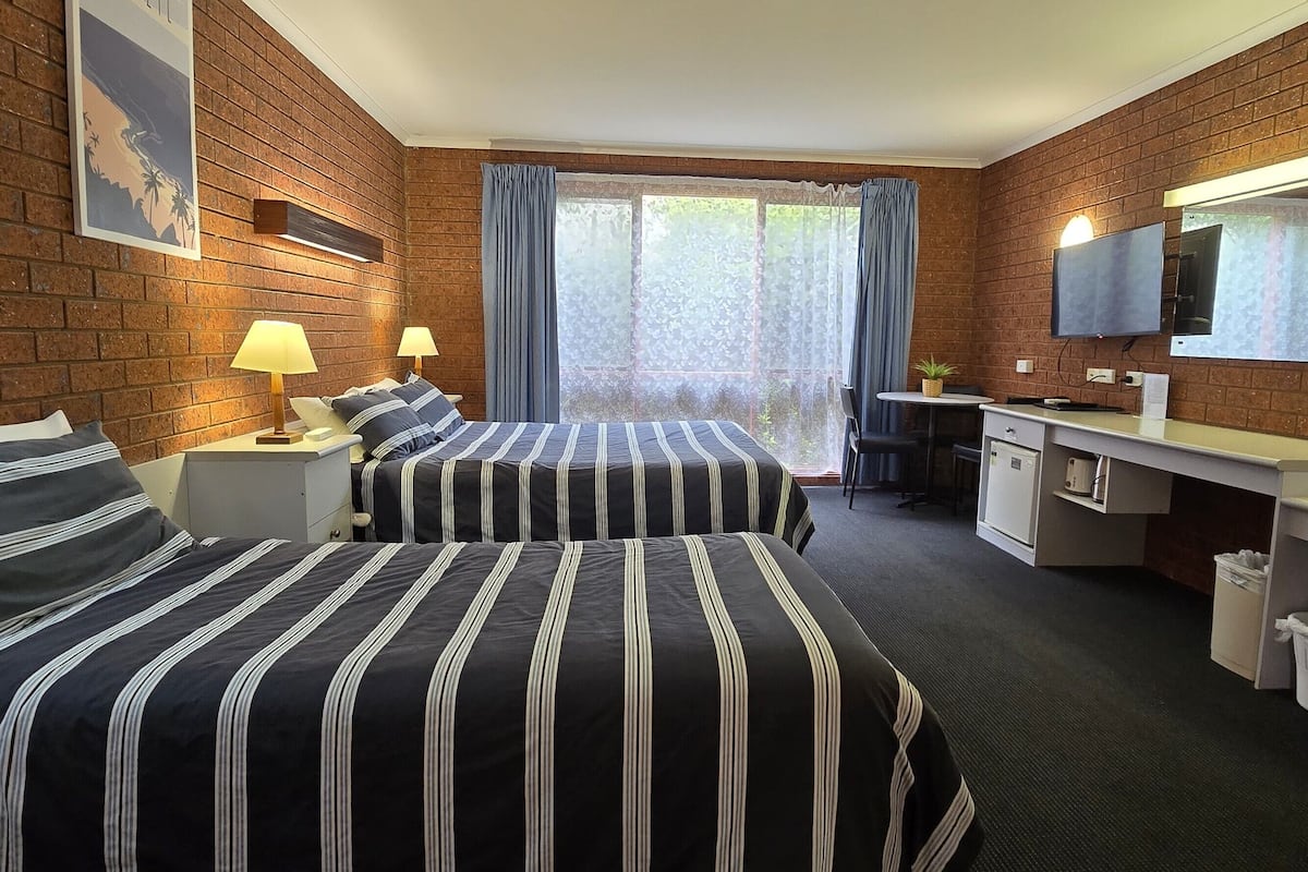 A hotel room with two beds, a desk, a TV, and a window with curtains.