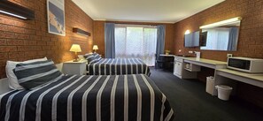 A hotel room with two beds, a desk, a TV, and a window with curtains.