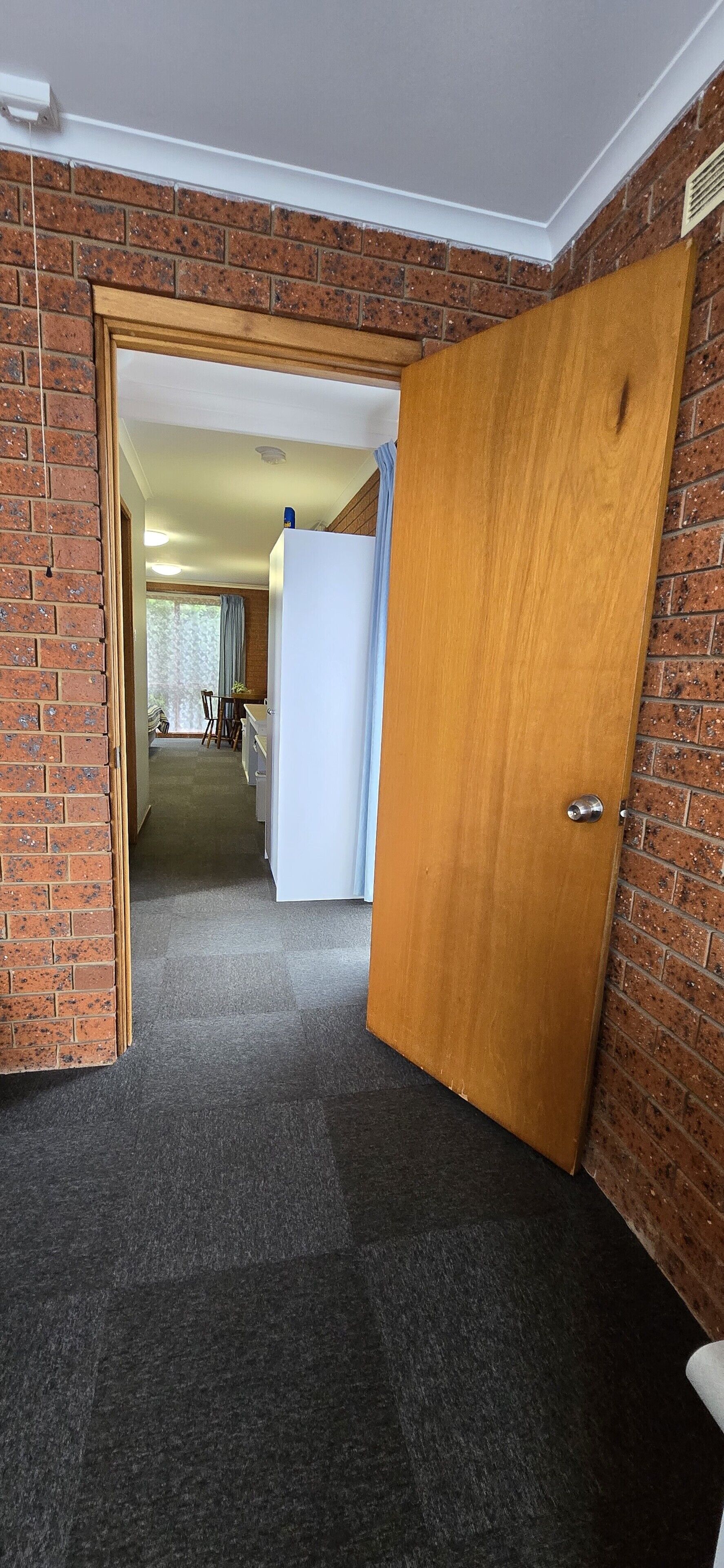 A hallway with a wooden door, carpeted floor, and brick walls.
