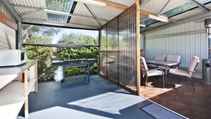 A covered outdoor patio with a grill, seating area, and a microwave on a shelf.