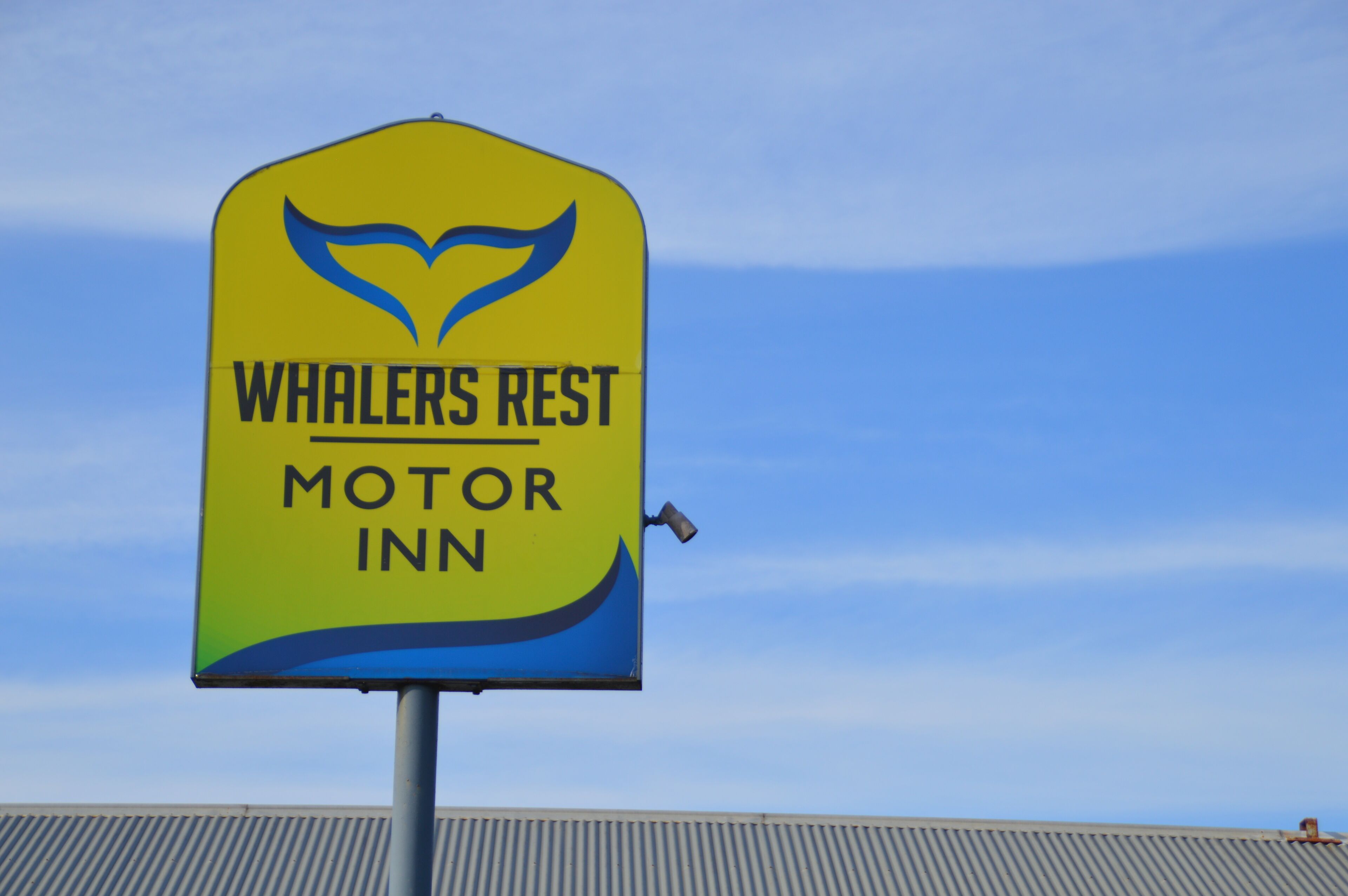 A yellow sign with the text "Whalers Rest Motor Inn" and a whale tail logo.