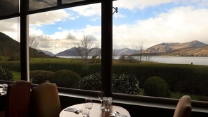 A dining table with chairs and a view of a lake and mountains through a window. - Ballachulish Hotel (Ballachulish)