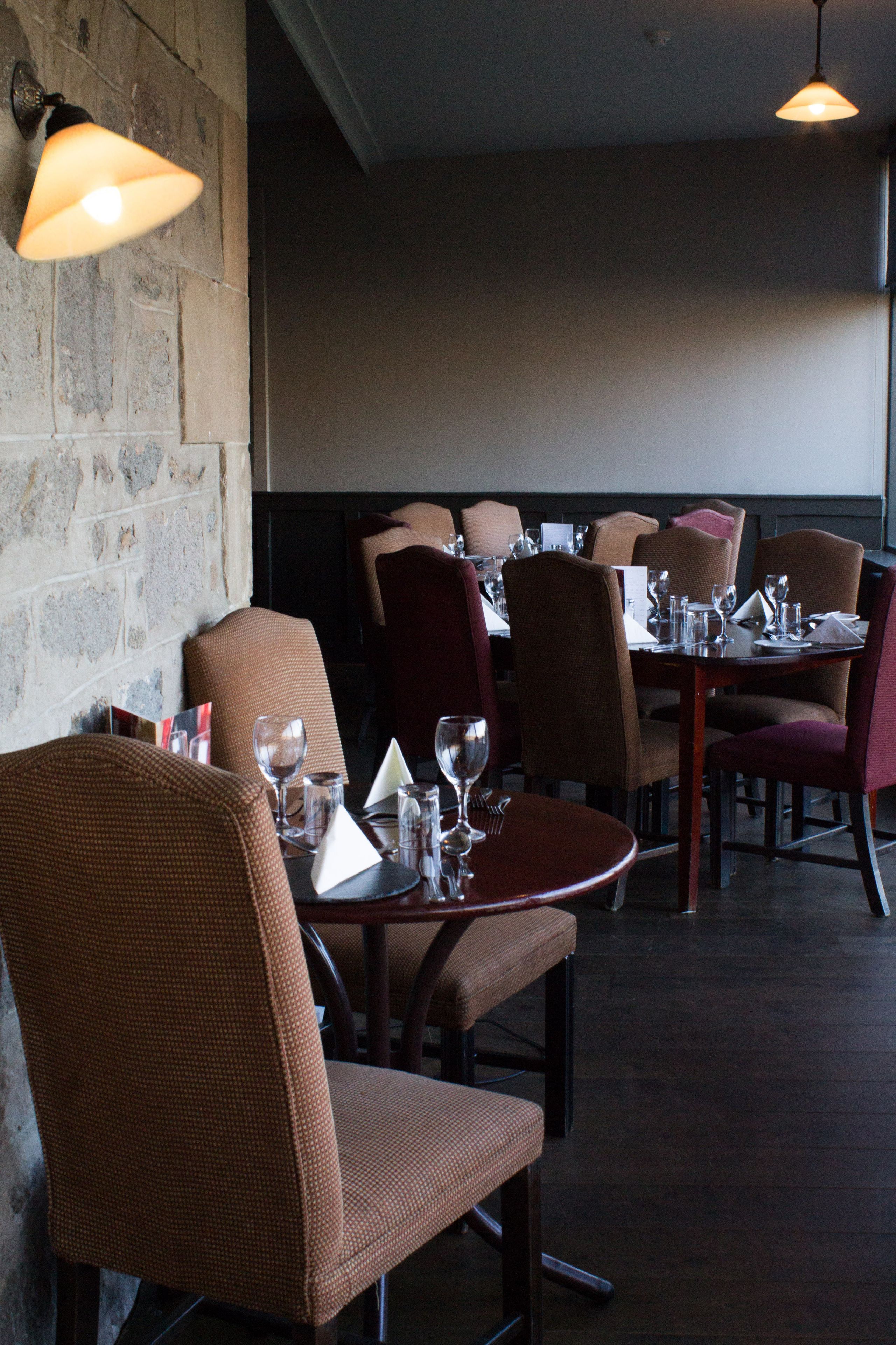 Interior de un restaurante con mesas y sillas de madera, paredes de piedra y lámparas colgantes.