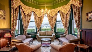 A room with a green wall, two sofas, a coffee table, and curtains with a floral pattern. - Ballachulish Hotel (Ballachulish)