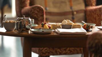 Una mesa de comedor con diversos alimentos para el desayuno, como pasteles, un tazón de cereal y una tetera.