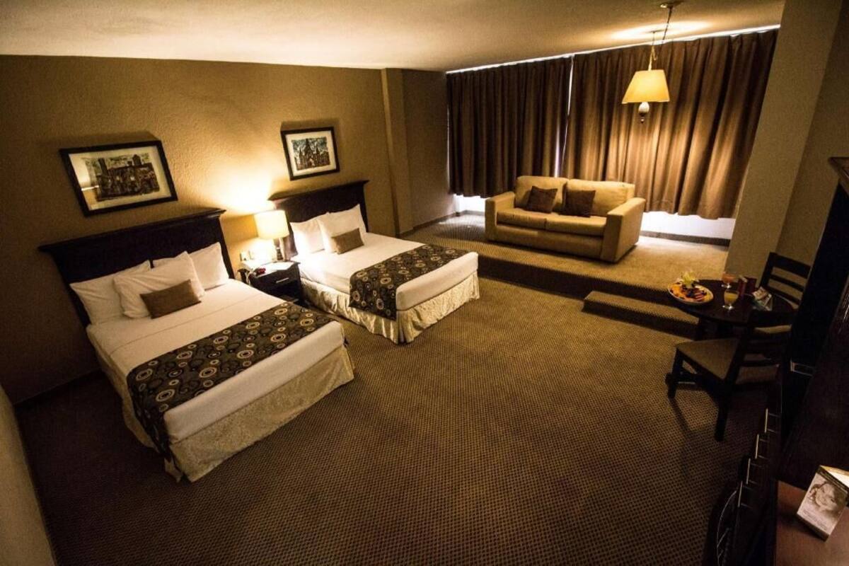 A hotel room with two beds, a sofa, a dining table, and a TV.