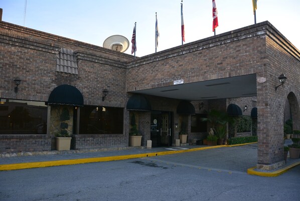 A brick building with a covered entrance, potted plants, and multiple flags.