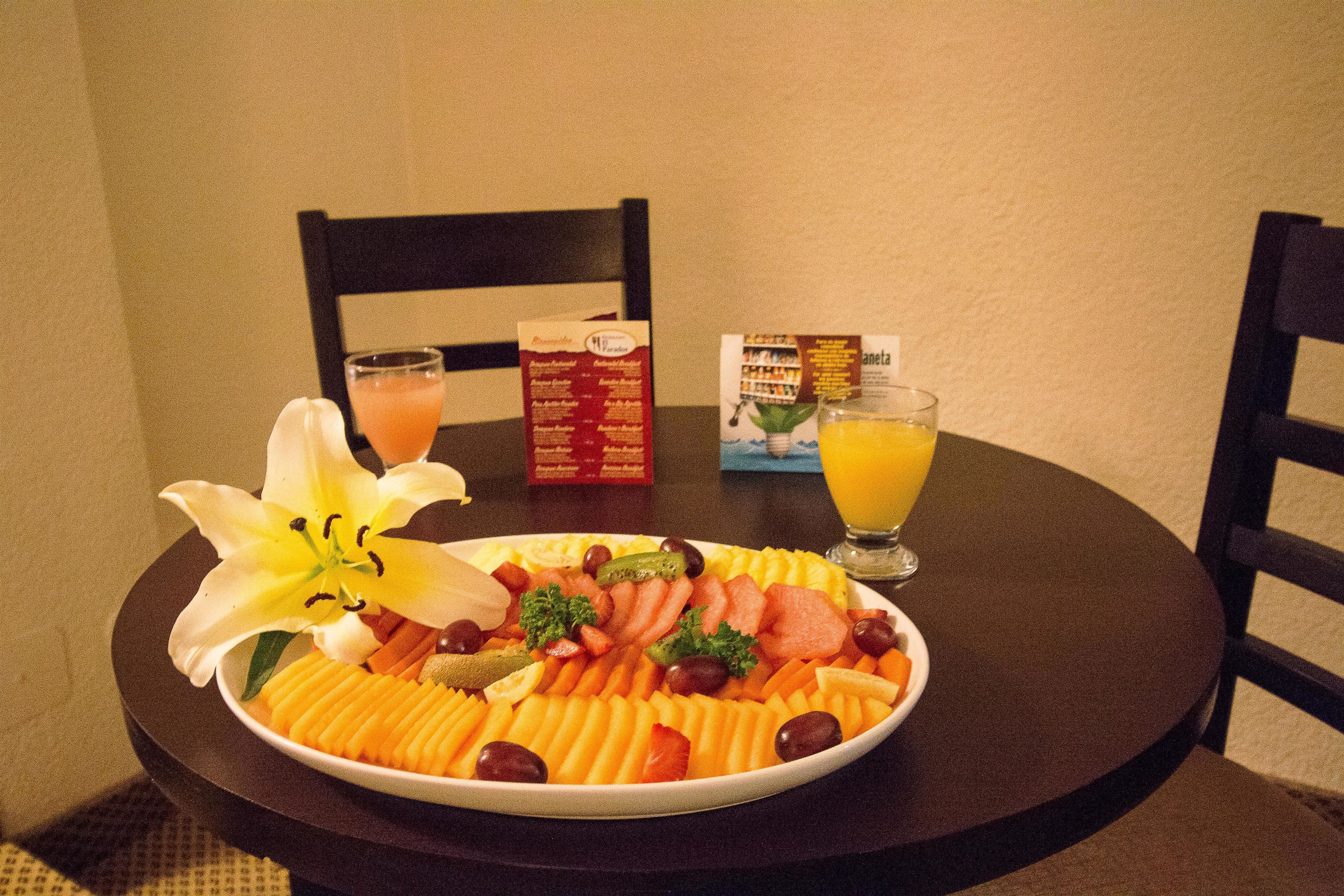 A table with a fruit platter, two glasses of orange juice, and a box of cereal.