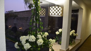 En korridor med en krukväxt med vita blommor, en hängande lampa och en tegelvägg med ett fönster.