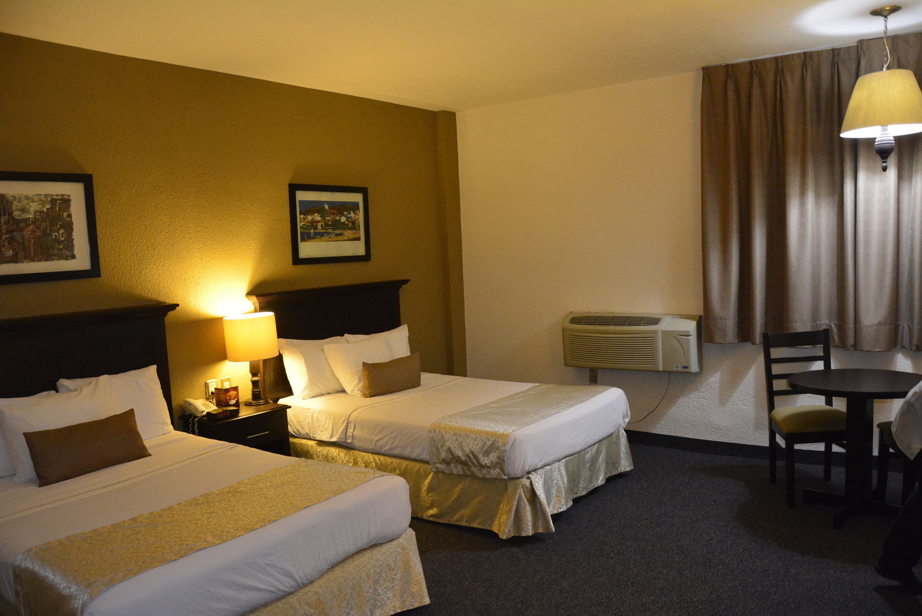 Habitación de hotel con dos camas, un escritorio, una silla y una lámpara.