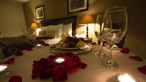 En romantisk middagsdukning med rosenblad, ljus och vinglas på ett bord i ett hotellrum.