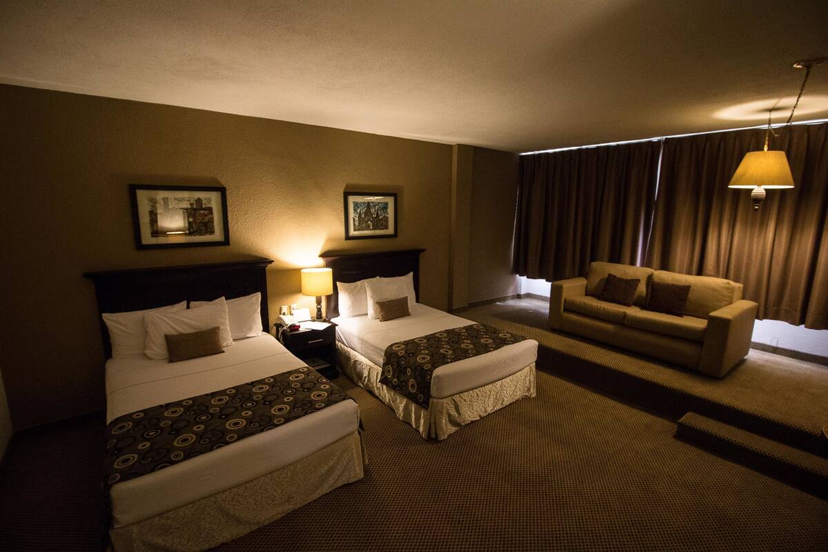 A hotel room with two beds, a sofa, and a large window with curtains.
