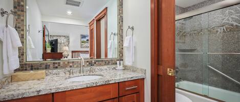 A bathroom with a granite countertop, wooden cabinets, a large mirror, and a glass-enclosed shower.