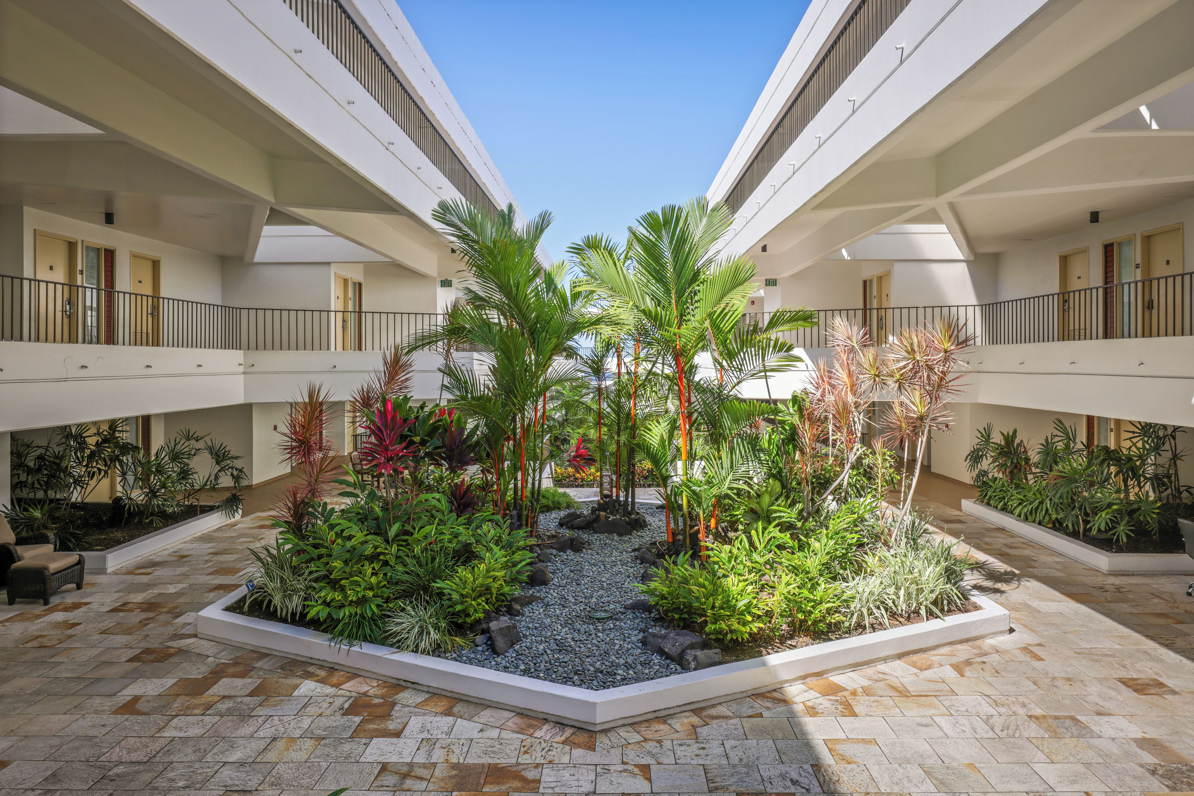 A modern hotel atrium with a central garden, multiple balconies, and a tiled floor.