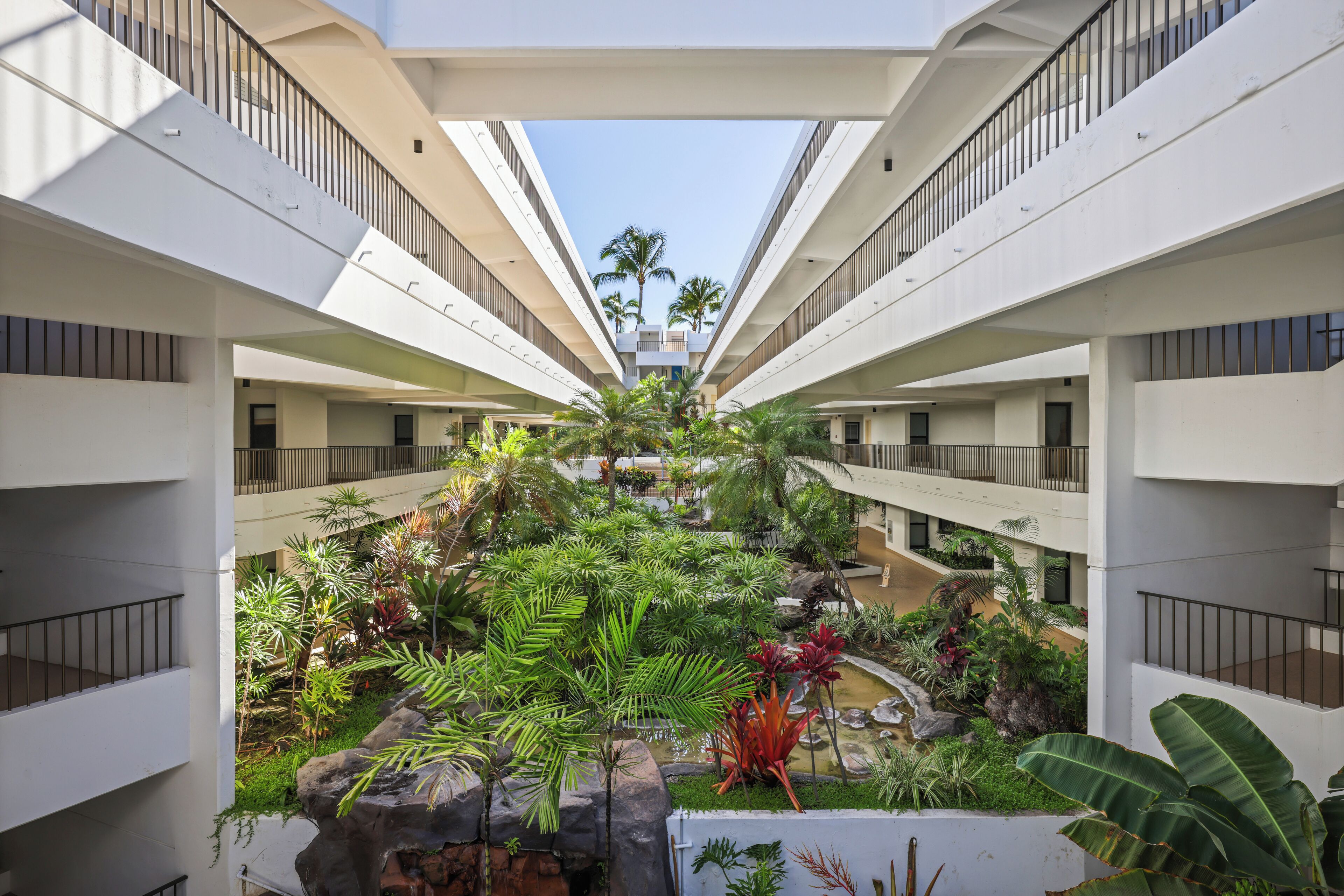 A multi-level atrium with a central garden, balconies, and a clear sky view.