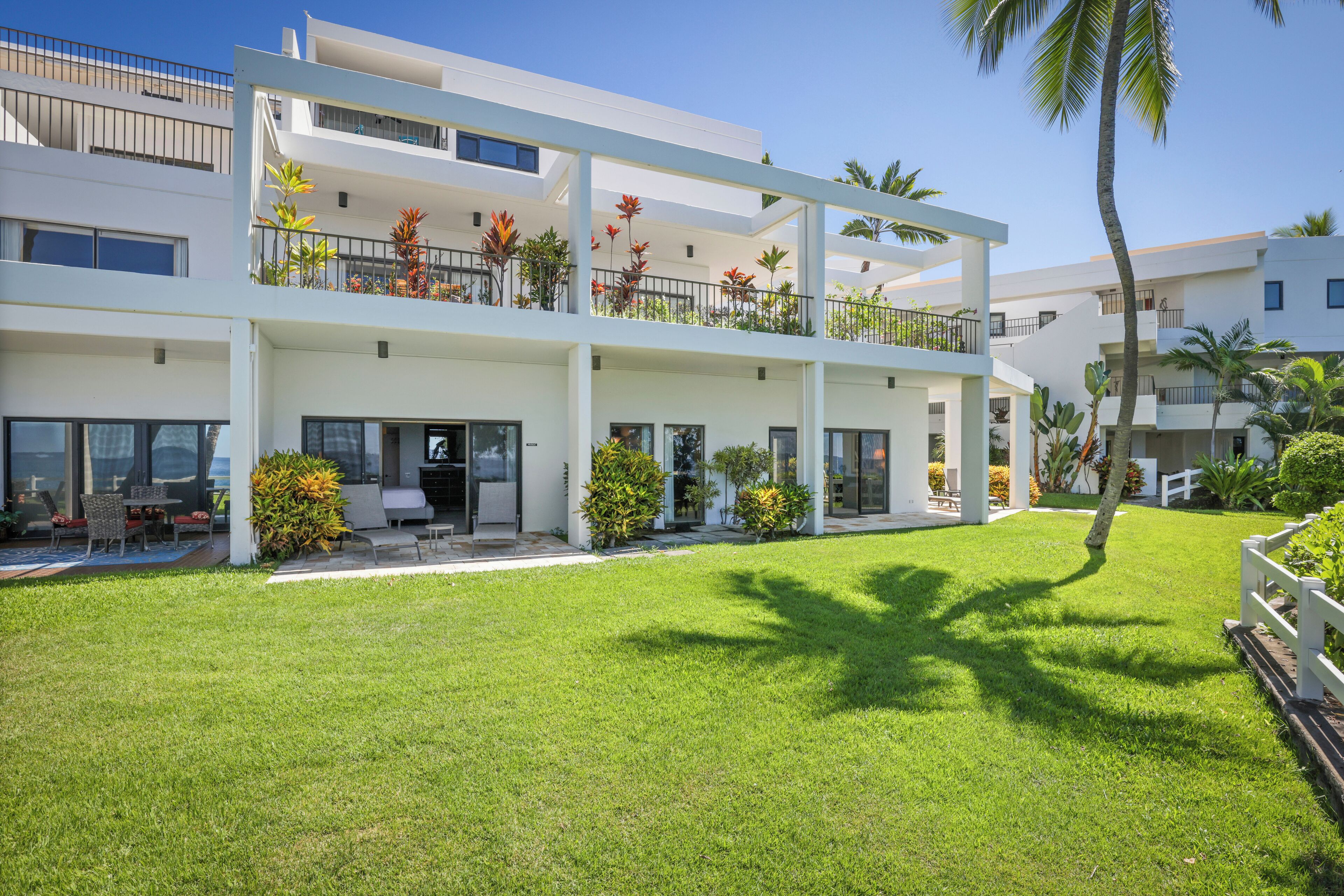 A modern multi-story building with balconies, outdoor seating, and a well-maintained lawn.