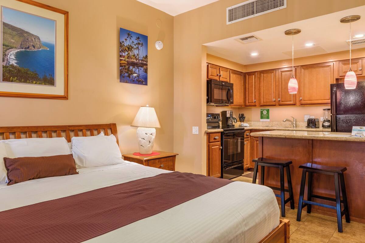 Une chambre d’hôtel avec un lit, une table de chevet, une lampe, une kitchenette et une vue sur l’océan.