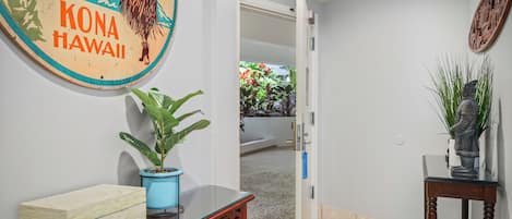 Un pasillo con una mesa de madera, una planta en maceta, un letrero decorativo y una estatua.