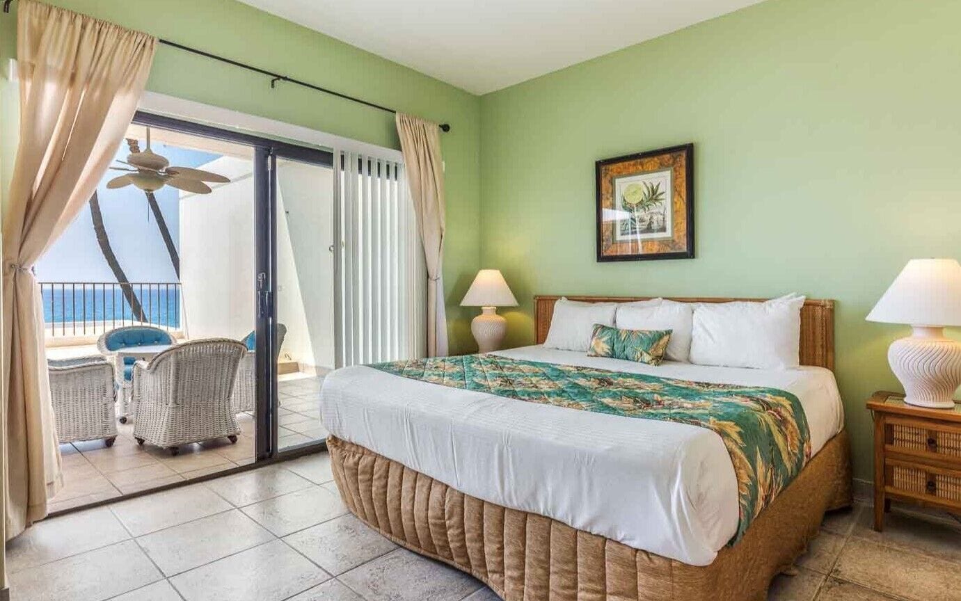 A bedroom with a bed, two bedside lamps, a window with curtains, a ceiling fan, and a framed picture on the wall.