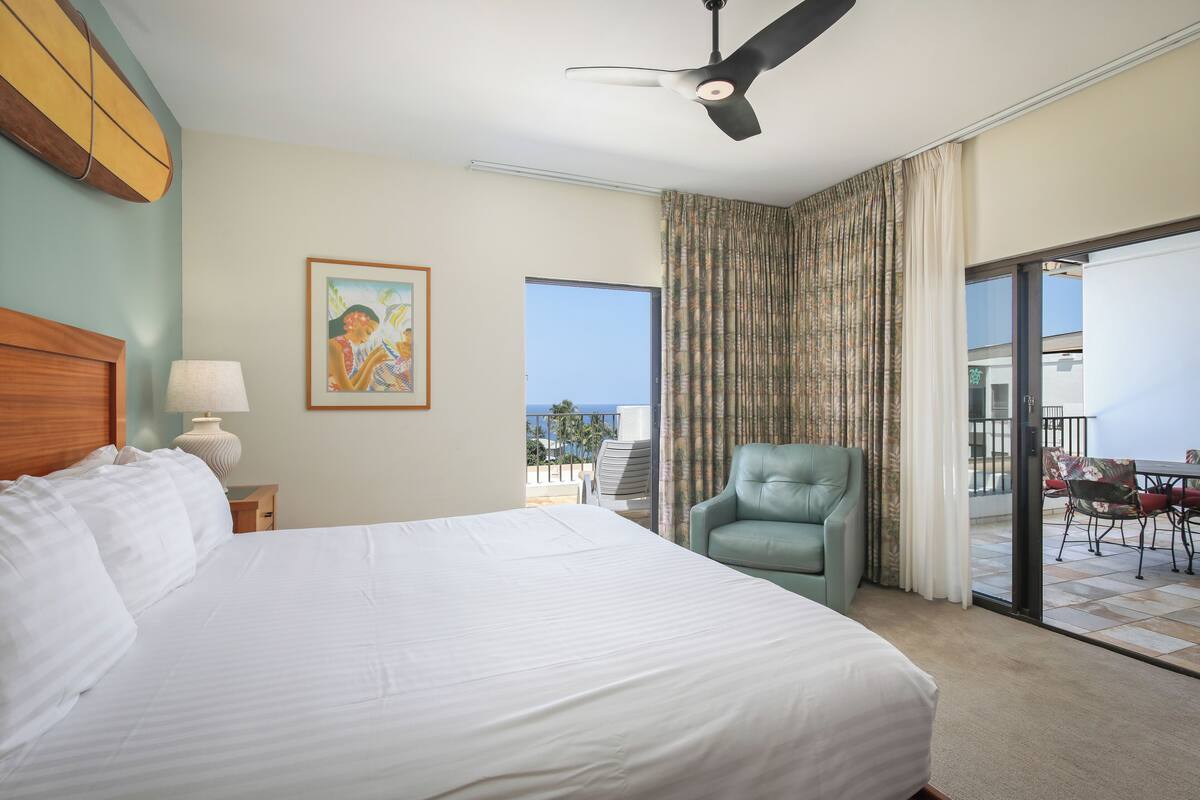 Une chambre d’hôtel avec un grand lit, un ventilateur de plafond, une fenêtre avec des rideaux, une chaise et une vue sur l’extérieur.