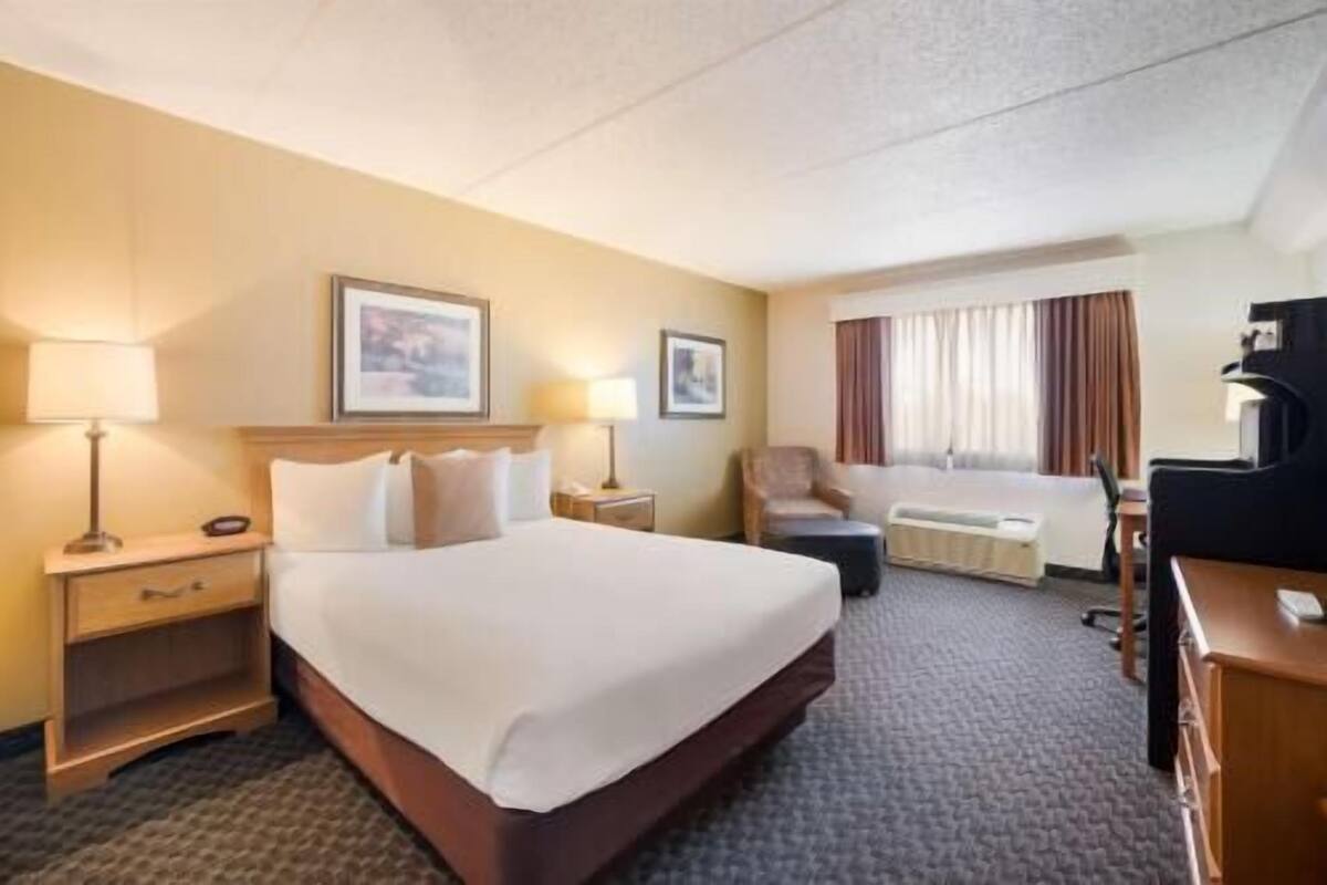 A hotel room with a large bed, bedside tables, a desk, a chair, and a window with curtains.