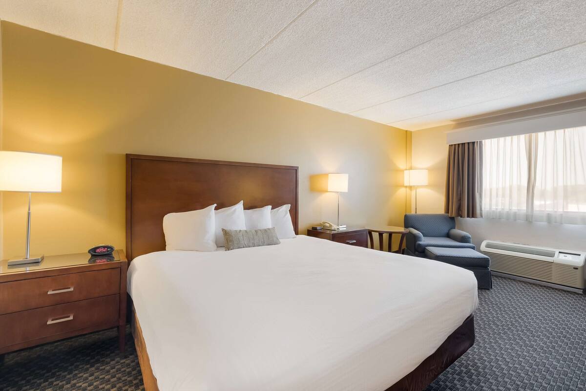A hotel room with a large bed, two bedside tables with lamps, a chair, and a window with curtains.