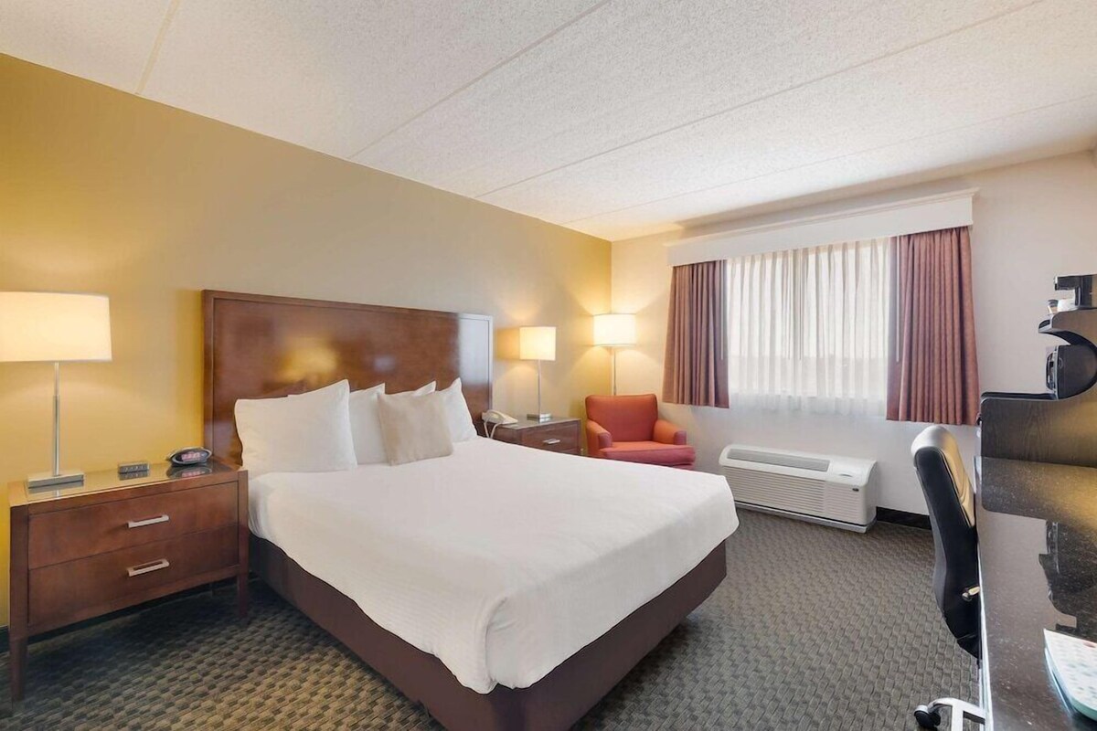A hotel room with a large bed, bedside tables, a desk, a chair, and a window with curtains.