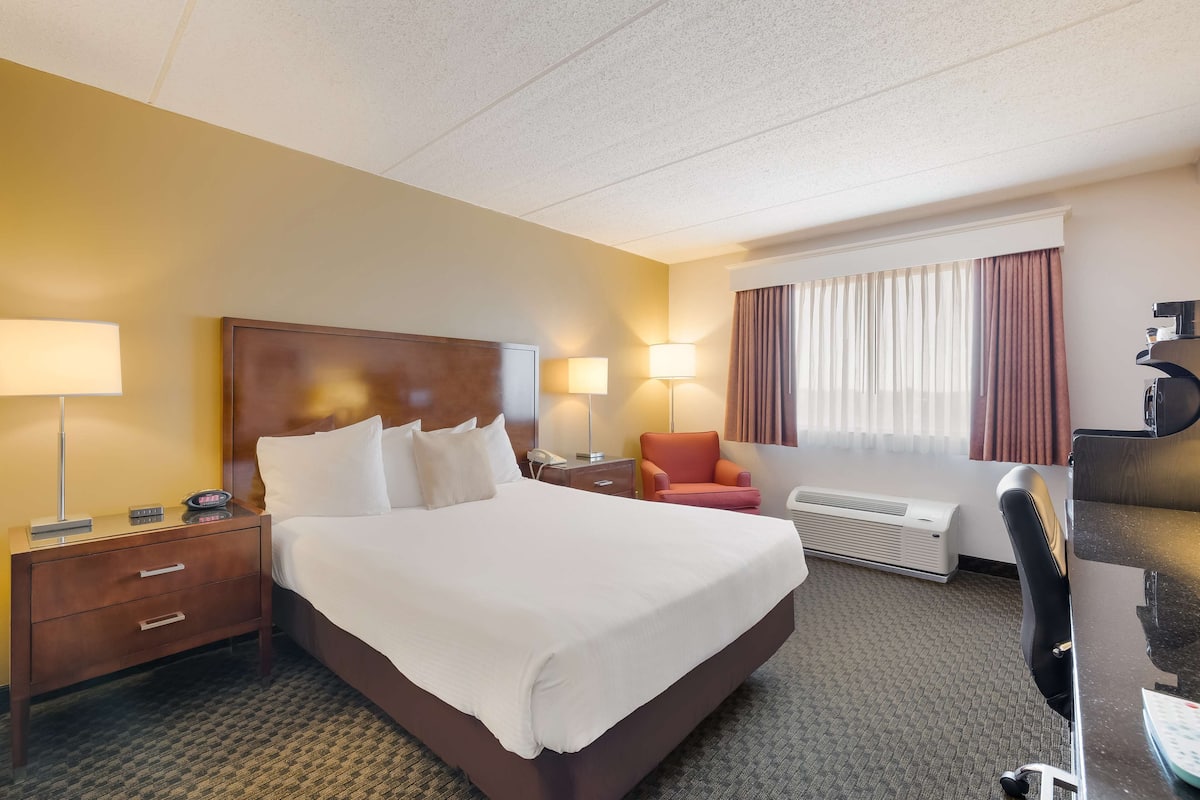 A hotel room with a large bed, a desk, a chair, a desk lamp, a telephone, and a window with curtains.