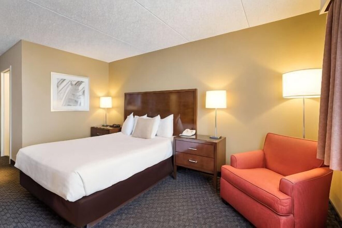 A hotel room with a bed, two bedside tables, a nightstand, a red armchair, and two wall-mounted lamps.