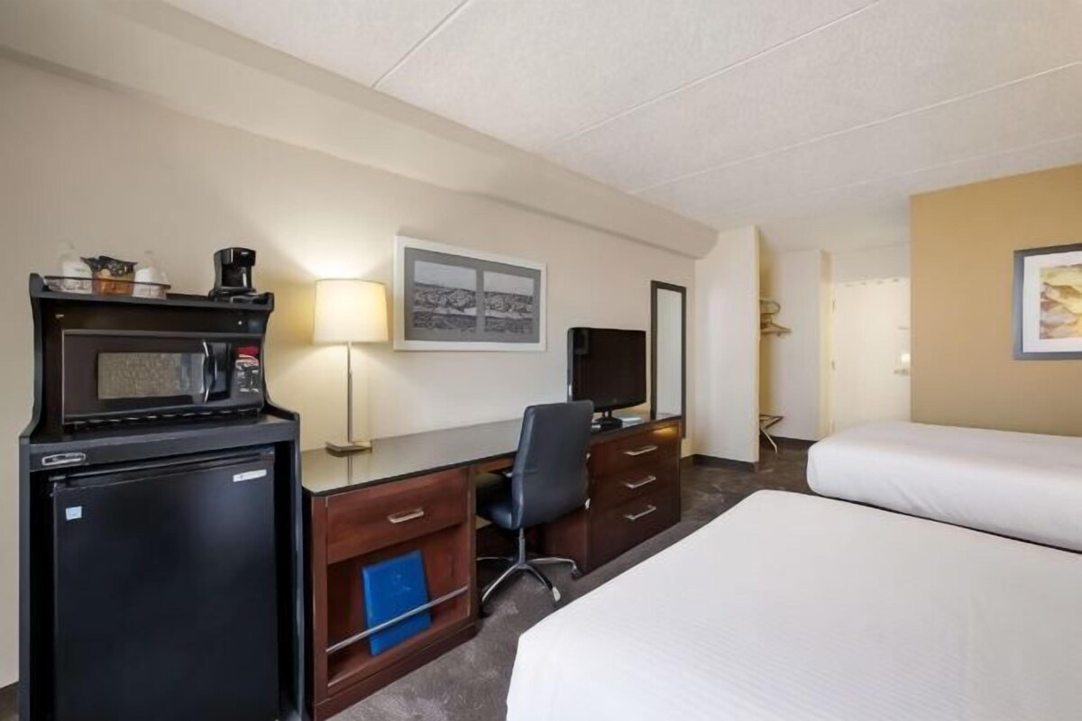 A hotel room with a bed, desk, microwave, refrigerator, and a television.