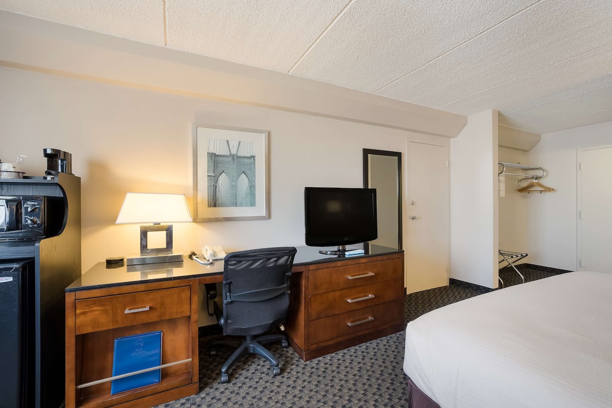 A hotel room with a desk, chair, television, and a bed.