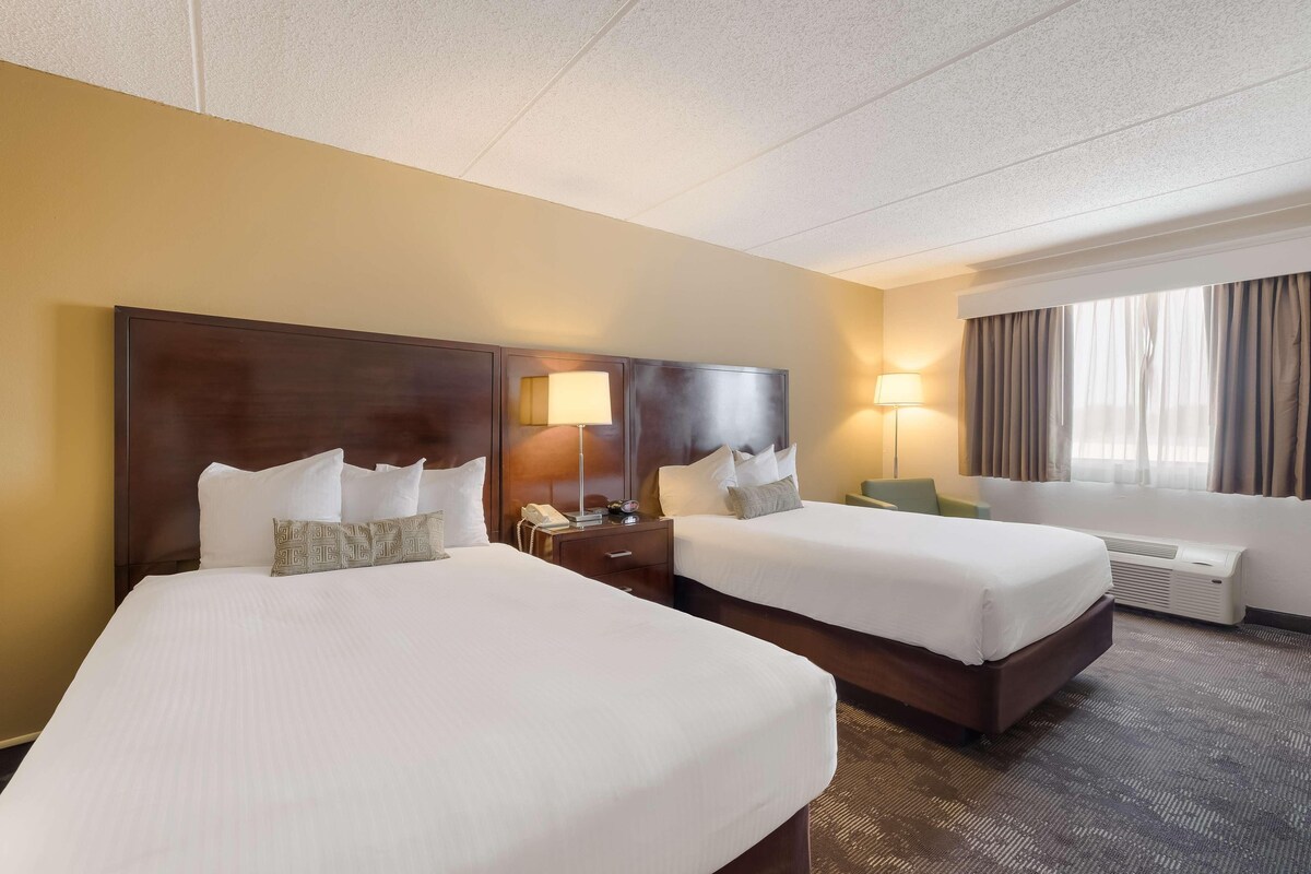 A hotel room with two beds, a desk, a lamp, a telephone, and a window with curtains.