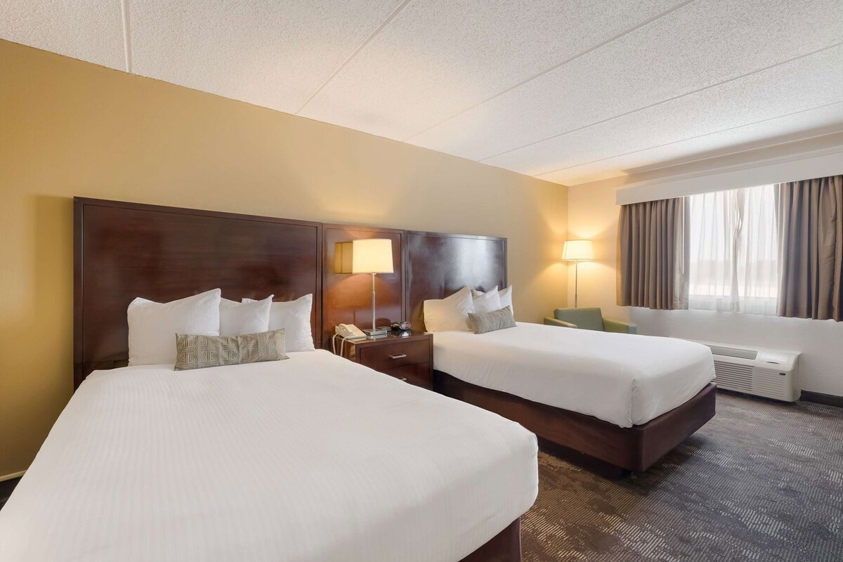 A hotel room with two beds, a desk, a lamp, a phone, and a window with curtains.
