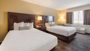 Een hotelkamer met twee bedden, een bureau met lamp, een telefoon en een raam met gordijnen.