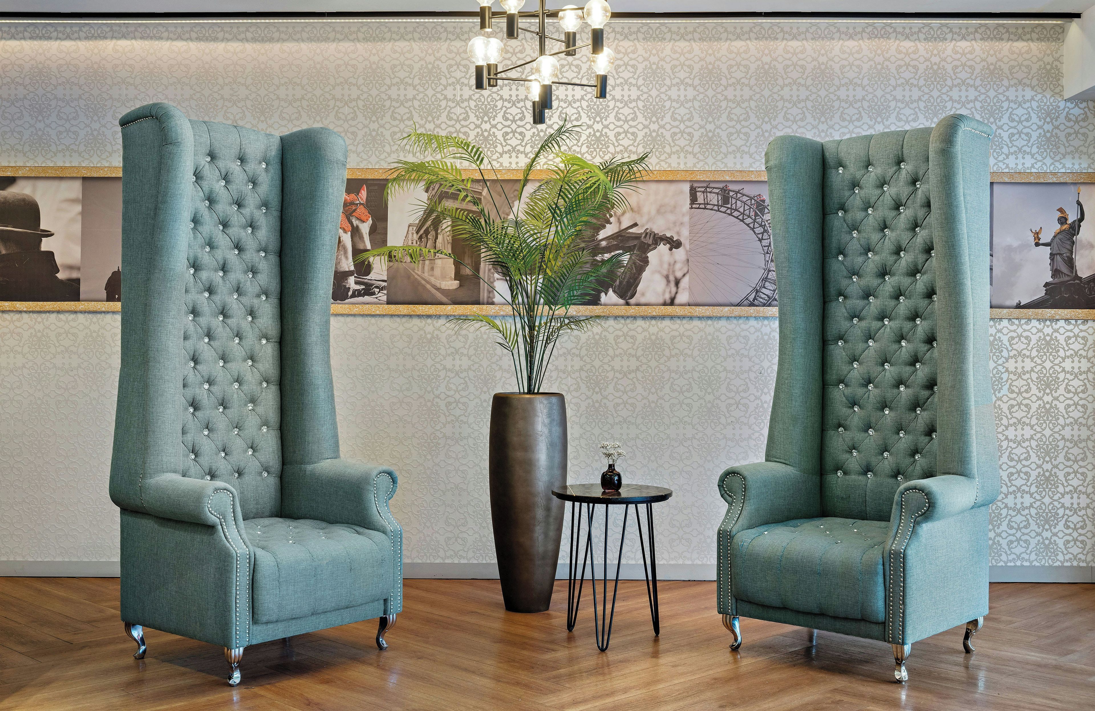 Zwei hohe Sessel mit gebuckelter Polsterung und Metallbeinen stehen auf einem Holzboden, dazwischen ein großer Blumentopf mit Grünpflanzen.