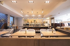 A modern restaurant with multiple dining tables and chairs, pendant lighting, and a kitchen area in the background. - Leonardo Hotel Vienna Westbahnhof (Vienna)