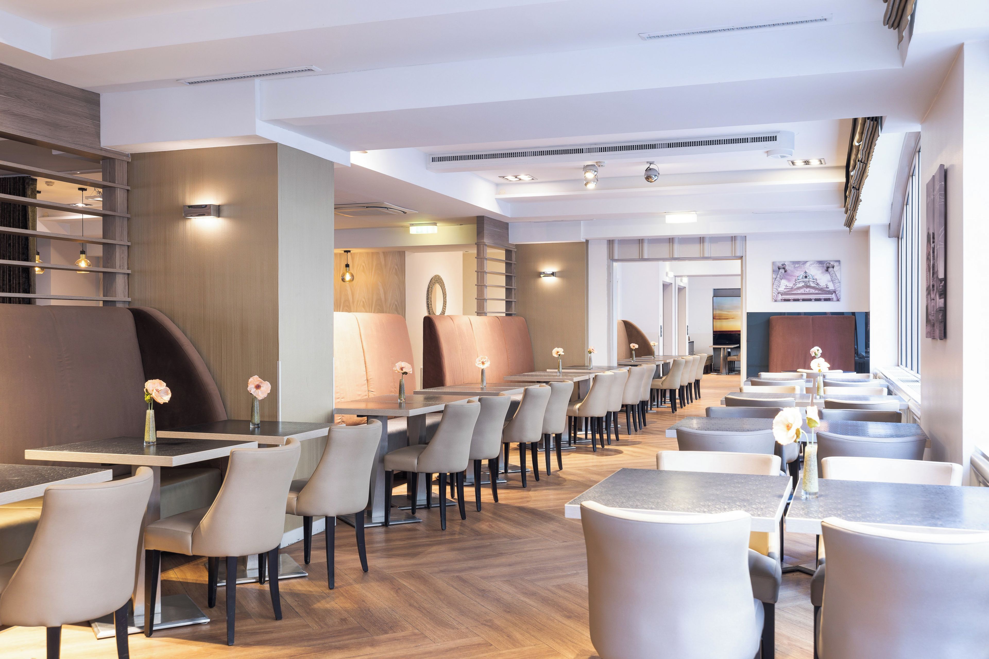 Un restaurant moderne doté de nombreuses tables et chaises, d’un plancher en bois et d’un escalier menant à un niveau supérieur.