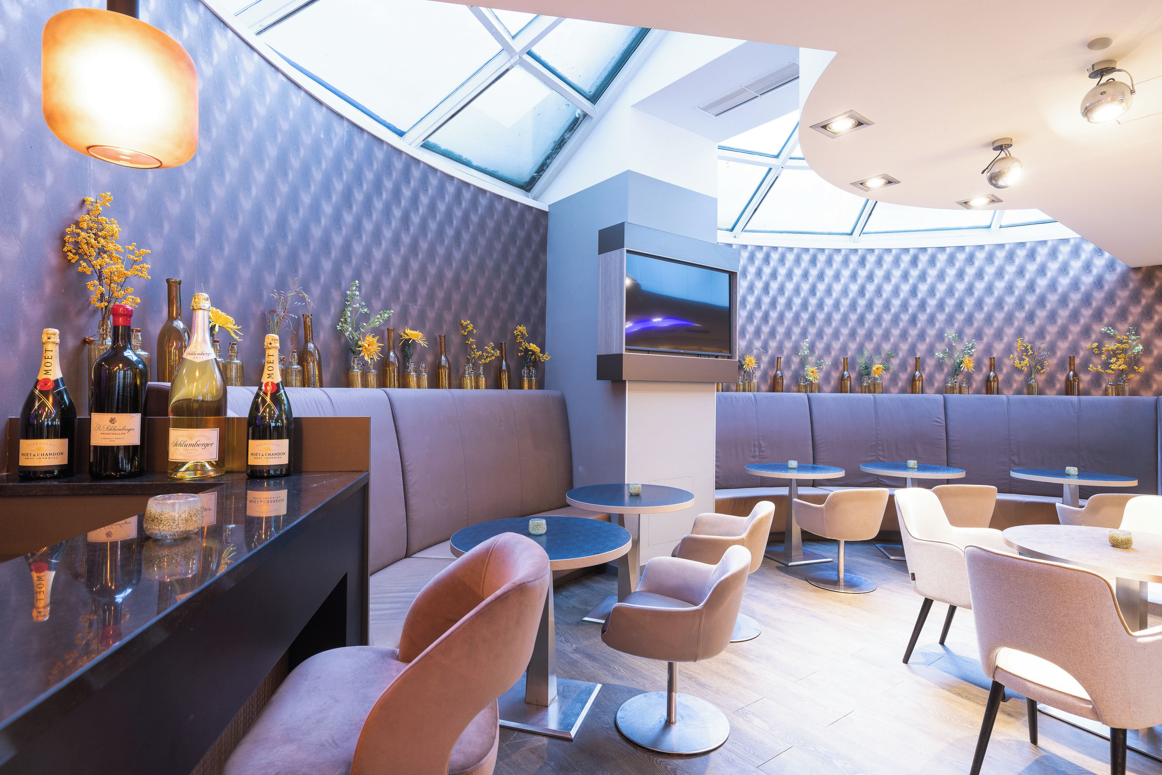A modern bar area with seating, a TV, and a variety of wine bottles.