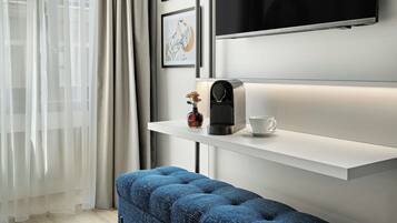 Quarto de hotel moderno com escrivaninha branca, máquina de café, xícara e um banco acolchoado azul.