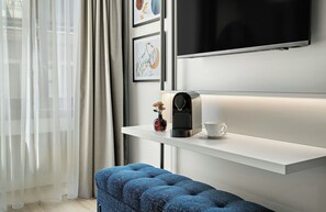 A modern hotel room with a white desk, a coffee machine, a cup, and a blue upholstered bench. - Leonardo Hotel Vienna Westbahnhof (Vienna)