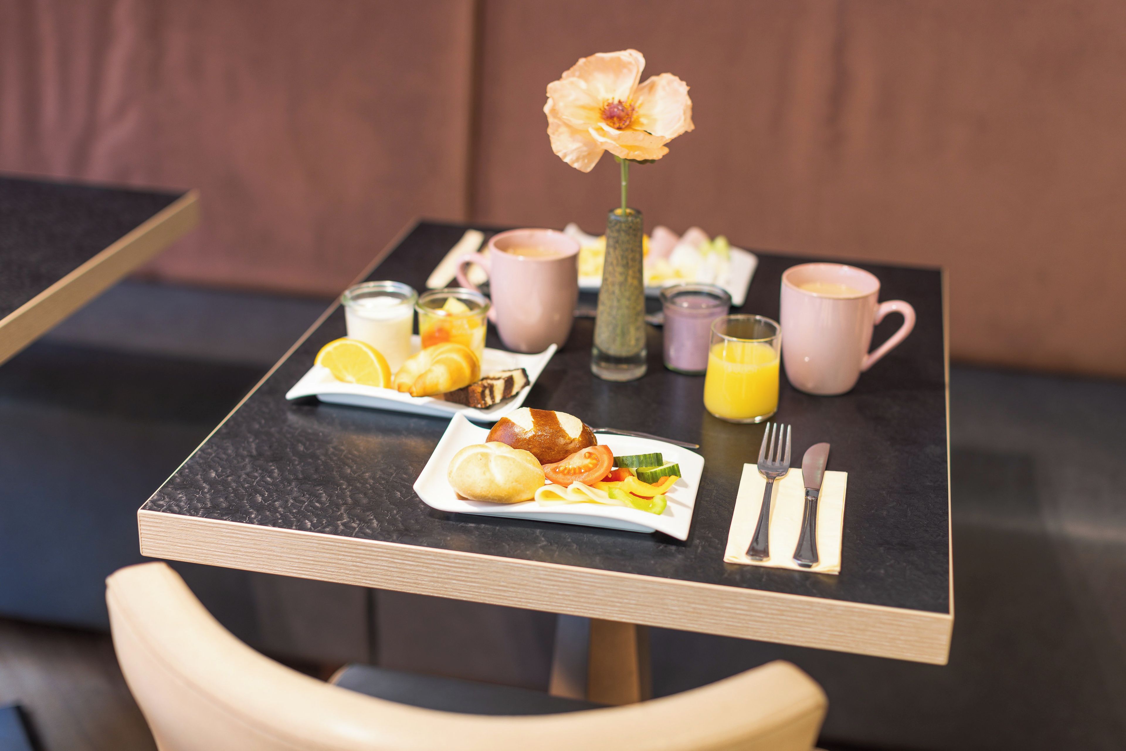 A breakfast table with a flower vase, a plate of food, a glass of orange juice, and a cup of coffee.