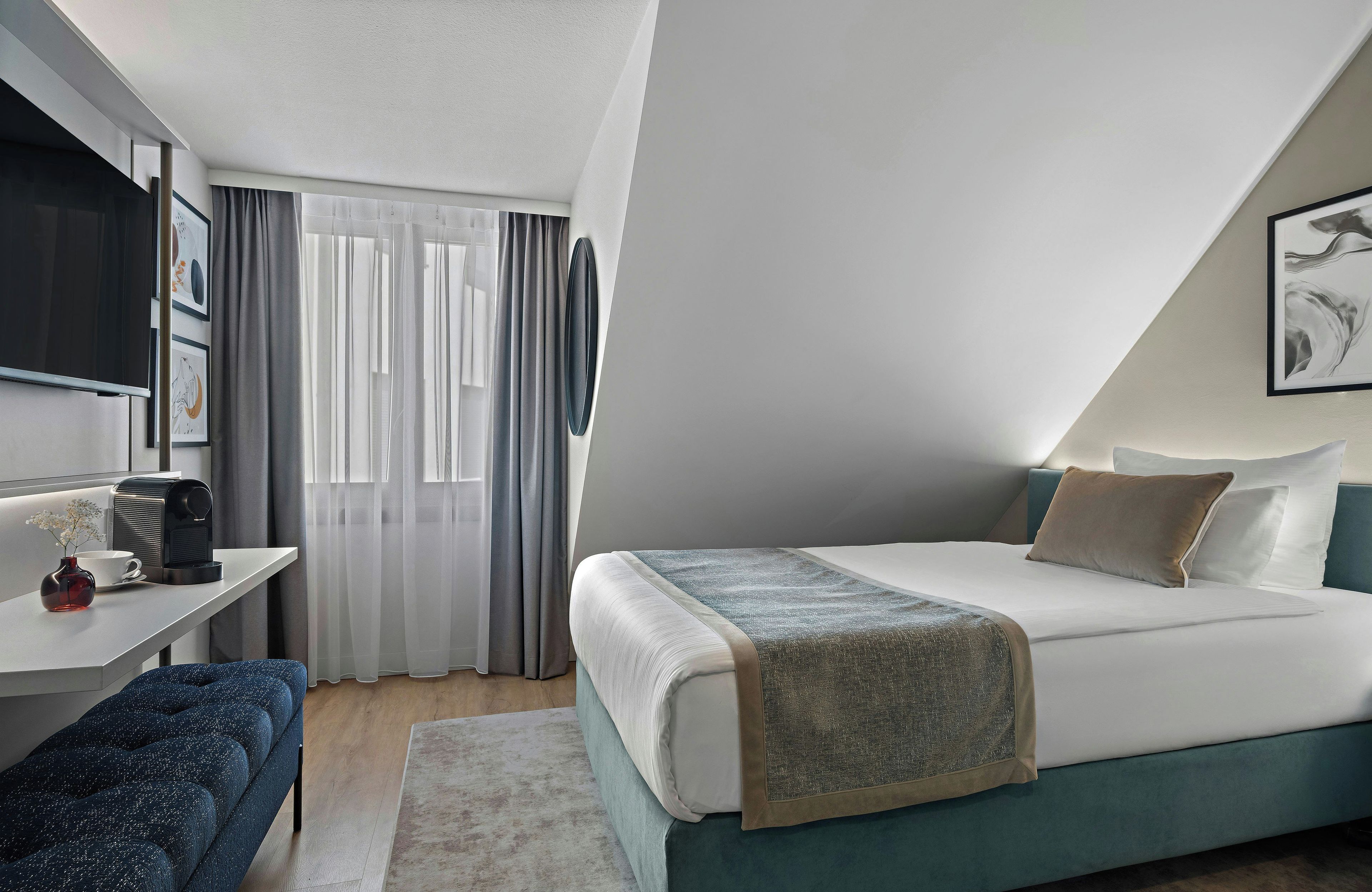 Una habitación de hotel moderna con cama, escritorio, cafetera y ventana con cortinas.