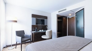 Una habitación de hotel moderna con una cama, un escritorio, una silla, un televisor y un armario.
