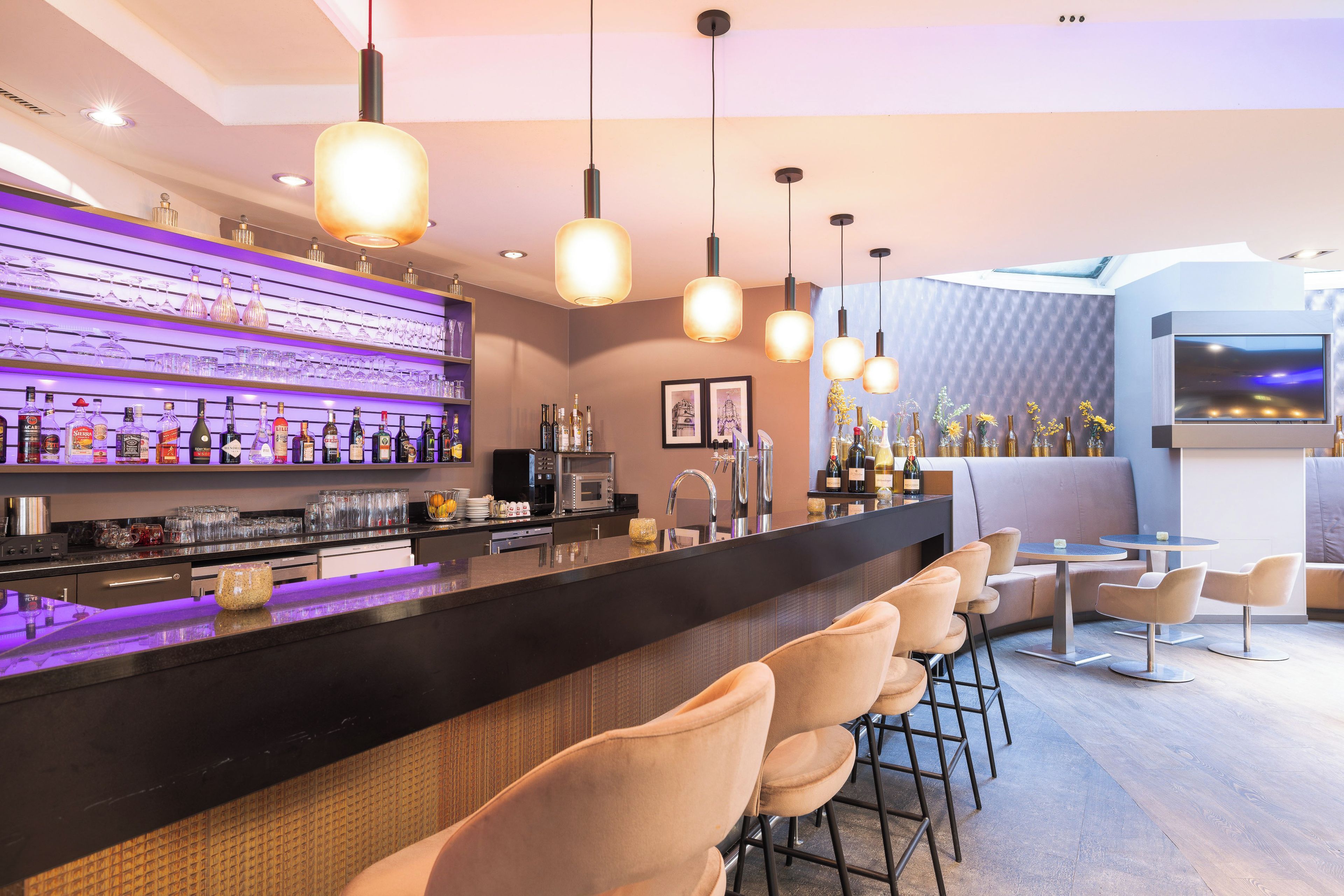 Eine moderne Bar mit einer schwarzen Arbeitsplatte, Barhocker und Pendelleuchten.