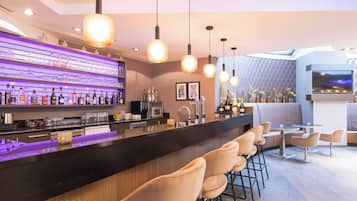 Eine moderne Bar mit einer schwarzen Arbeitsplatte, Barhocker und Pendelleuchten.