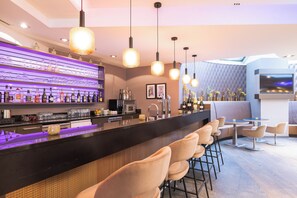 A modern bar area with a black countertop, bar stools, and pendant lighting. - Leonardo Hotel Vienna Westbahnhof (Vienna)