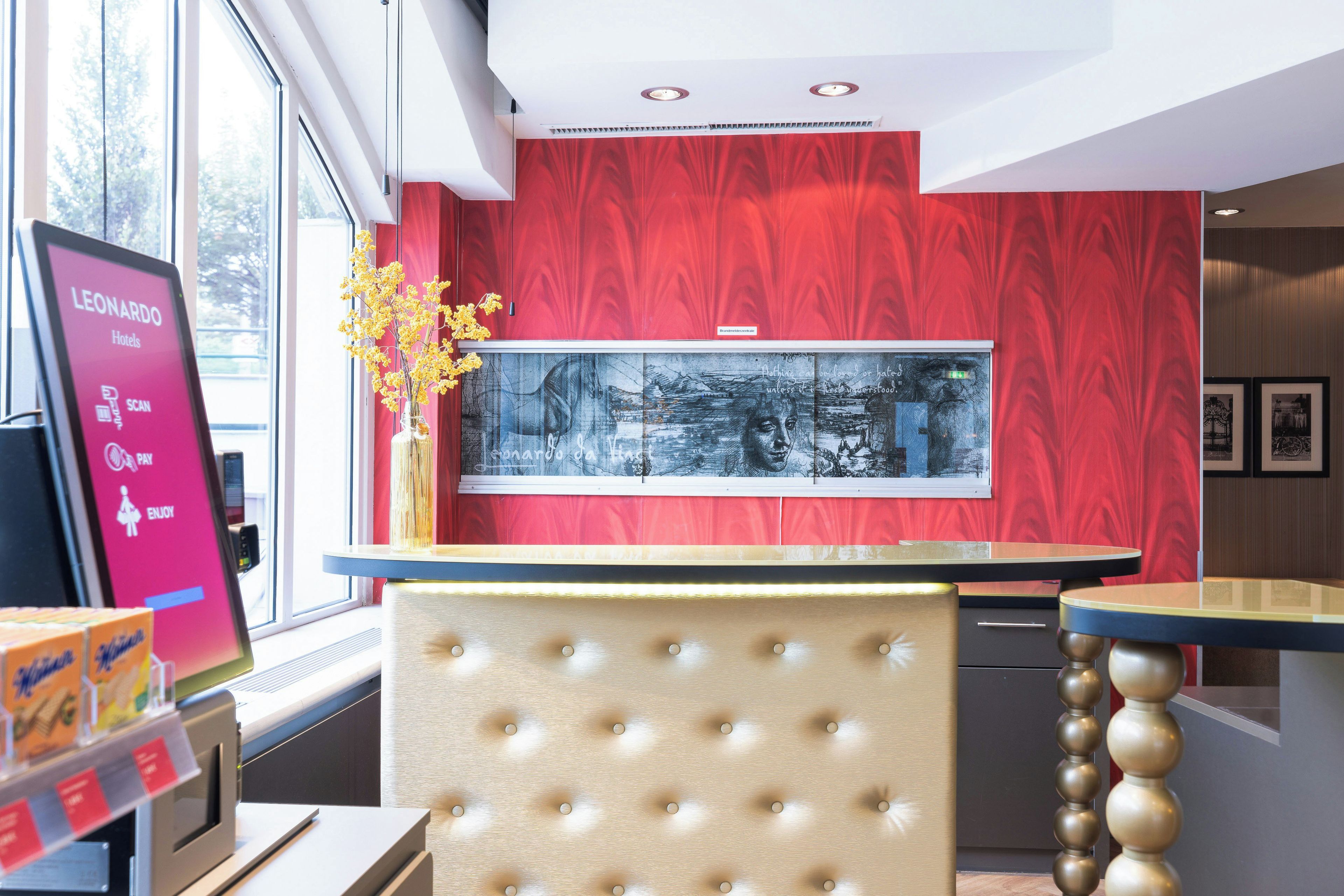 Ein Hotel-Empfangsbereich mit roter Wand, einem großen gerahmten Kunstwerk und einer modernen Rezeption.
