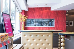 Een hotel receptie met een rode wand, een groot kunstwerk in een lijst en een modern receptiebalie.
