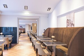 Un restaurante moderno con mesas largas y cabinas acolchadas, suelo de madera y un cuadro grande en la pared.