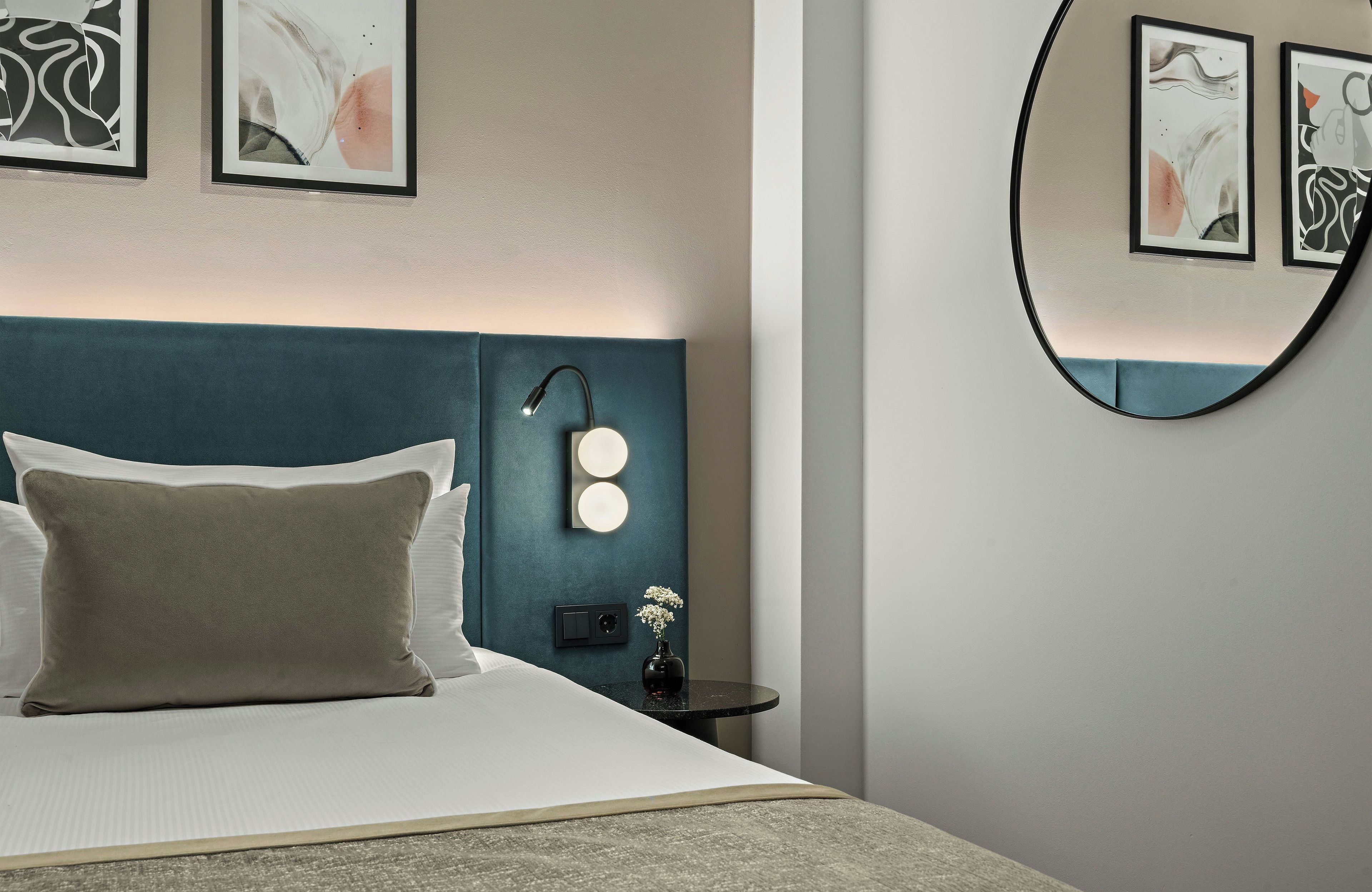 A neatly made bed with pillows, a bedside table with a lamp, and wall-mounted lights.